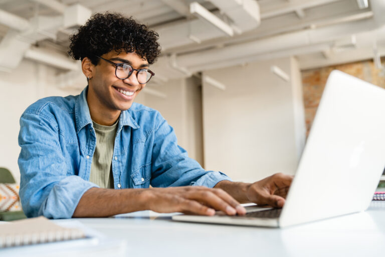 Happy smiling afro businessman using laptop at the desk in office